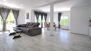 Un amplio salón con un sofá gris, una mesa de centro de cristal y una mesa de comedor con sillas.