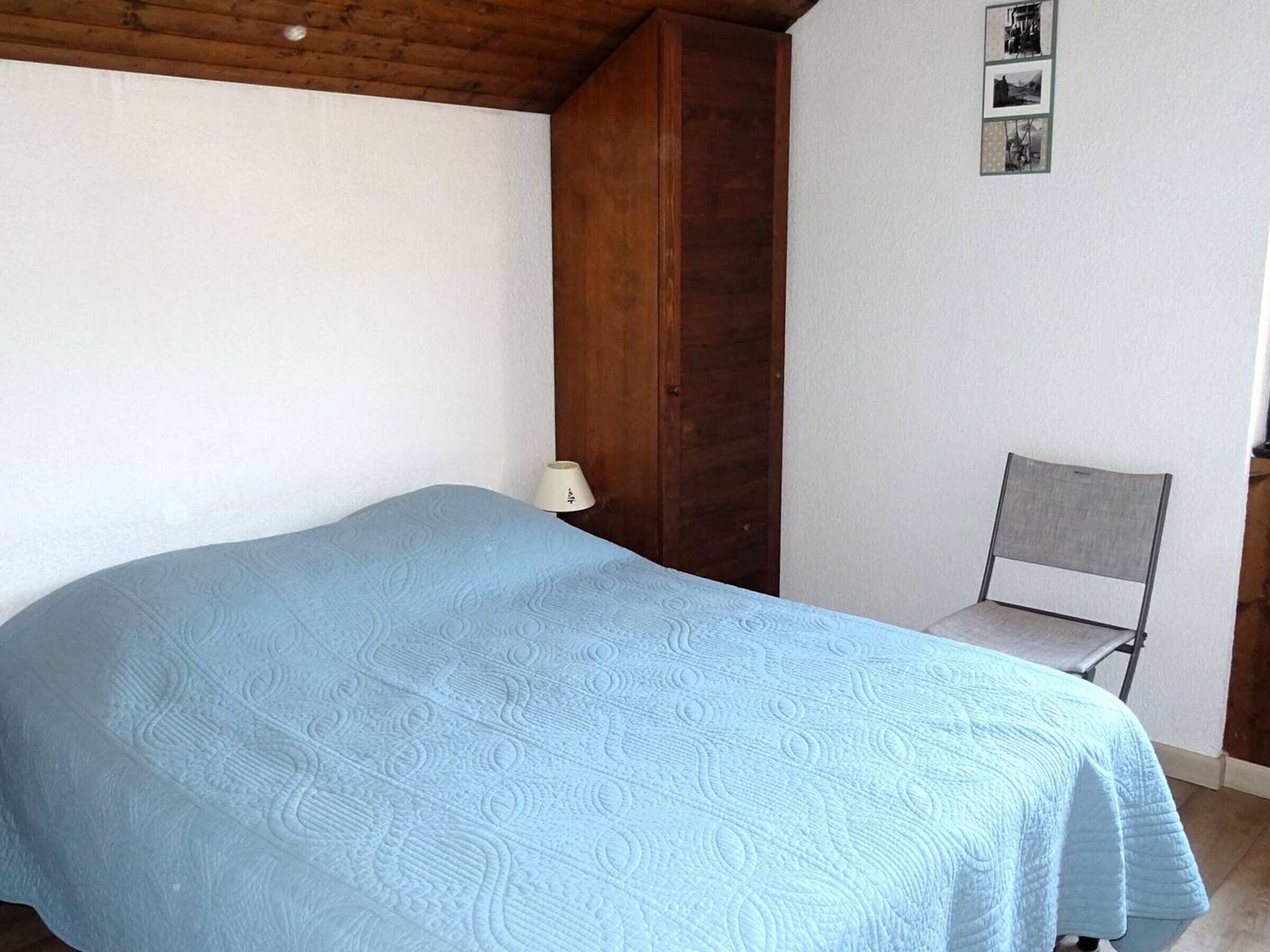 Ein Schlafzimmer mit einem Bett, einem Sessel, einem Holzschrank und einer Wand mit gerahmten Bildern.
