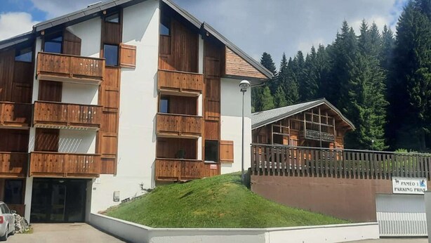 A multi-story building with wooden balconies, a parking area, and a sign indicating private parking. - Duplex 2BR for 5 - Ski-In/Ski-Out, Garage, Free Shuttle (Les Gets)