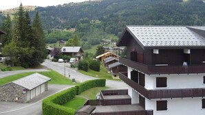 A multi-story building with balconies, a stone structure, and a view of a valley with houses and trees. - Duplex 2BR for 5 - Ski-In/Ski-Out, Garage, Free Shuttle (Les Gets)