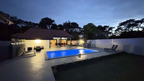 Ein Garten mit Schwimmbecken, Sitzgelegenheiten im Freien und einer überdachten Terrasse.