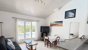 A modern living room with a sofa, a coffee table, a TV, and a dining area with chairs and a table. - Elegant modern villa steps from the beach (Biscarrosse Plage)