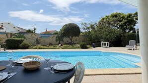 A dining area with a table set for two, overlooking a swimming pool. - Elegant modern villa steps from the beach (Biscarrosse Plage)