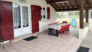 A covered patio with a table and chairs, red shutters, and a view of the outdoors. - Renovated villa near the lake, Biscarrosse (Biscarrosse)