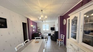 A dining area with a long table, chairs, a chandelier, a television, and a cabinet with glass doors. - Renovated villa near the lake, Biscarrosse (Biscarrosse)