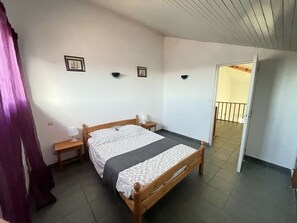 A bedroom with a wooden bed, two bedside tables, a window with curtains, and a door leading to another room. - Bright villa near the beach for 8 people (Biscarrosse Plage)