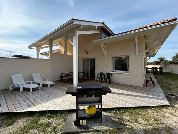 A covered outdoor patio with a grill, white chairs, and a table. - Bright villa near the beach for 8 people (Biscarrosse Plage)