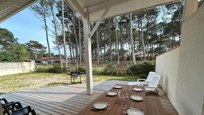 Un espacio comedor al aire libre techado, con una mesa de madera dispuesta para cuatro personas, rodeada de sillas blancas.