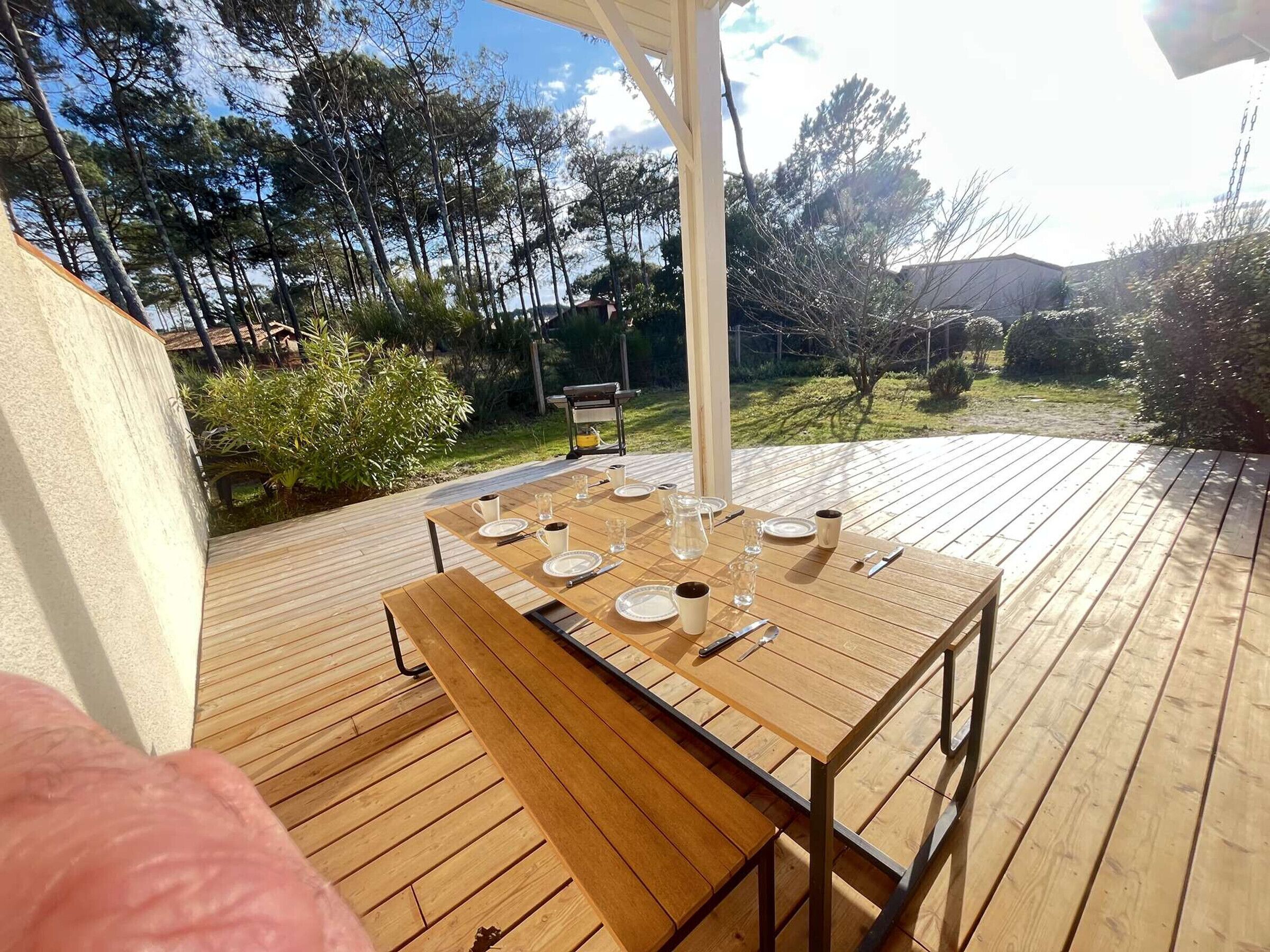 A wooden deck with a table set for dining, surrounded by trees and a garden.