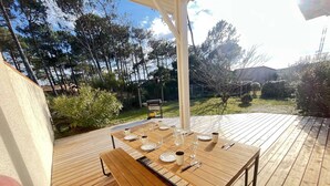 A wooden deck with a table set for dining, surrounded by trees and a garden. - Spacious Villa Near Beach, 8 People (Biscarrosse Plage)