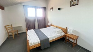 A bedroom with a wooden bed, a chair, a bedside table, and a window with curtains. - Spacious Villa Near Beach, 8 People (Biscarrosse Plage)
