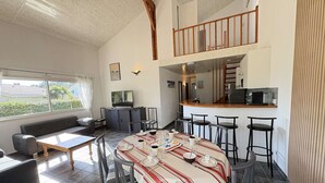 A modern kitchen with a bar area, a dining table set for four, and a loft bedroom with a balcony. - Spacious Villa Near Beach, 8 People (Biscarrosse Plage)