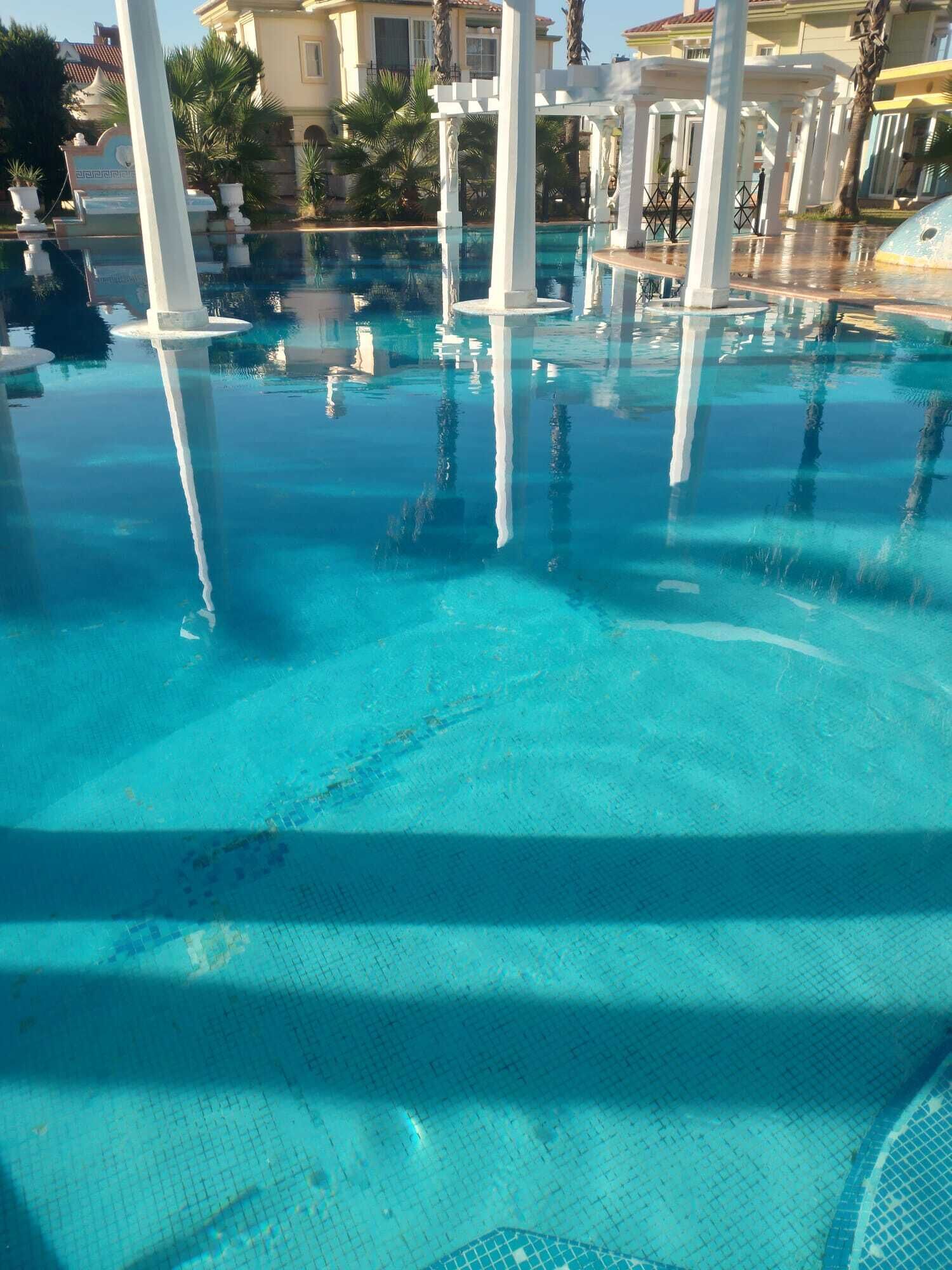 Une piscine d’un bleu éclatant, bordée de colonnes blanches et dotée d’une terrasse carrelée.