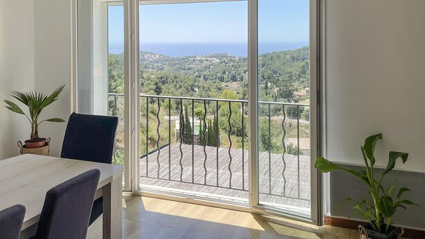 Un balcon donnant sur un paysage côtier, un coin repas avec une table et des chaises, et deux plantes en pot.