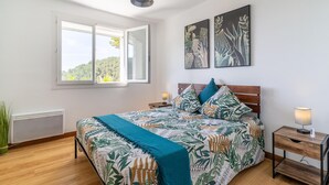 Une chambre à coucher comprenant un lit, une table de chevet, un radiateur, une fenêtre et deux œuvres d’art accrochées au mur.