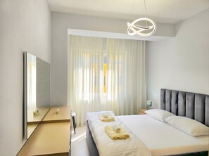 A modern hotel room with a large bed, a bedside table, a mirror, and a hanging light fixture.