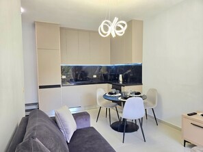 Uma sala de estar moderna com sofá, mesa de jantar com cadeiras, área de cozinha com bancada preta e luminária pendente.
