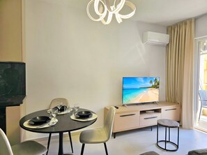Een moderne woonkamer met een eettafel gedekt voor twee personen, een televisie op een standaard, een bank en een raam met gordijnen.