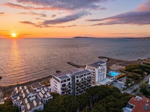 A coastal hotel with multiple floors, a swimming pool, and a pier extending into the sea.