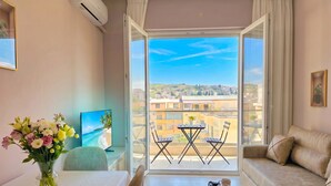 A room with a balcony, a dining table with chairs, a sofa, and a TV.