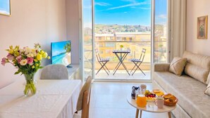 A modern living room with a balcony, a dining table with a vase of flowers, a sofa, and a TV. - Apartment by the Sea in Golem 095 (Durres)
