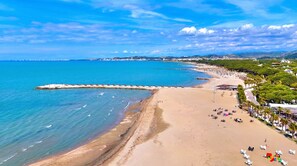 A coastal beach with a rocky breakwater, clear blue waters, and a sandy shore.