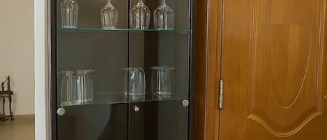 A dark wooden cabinet with glass doors and shelves, containing clear glassware.