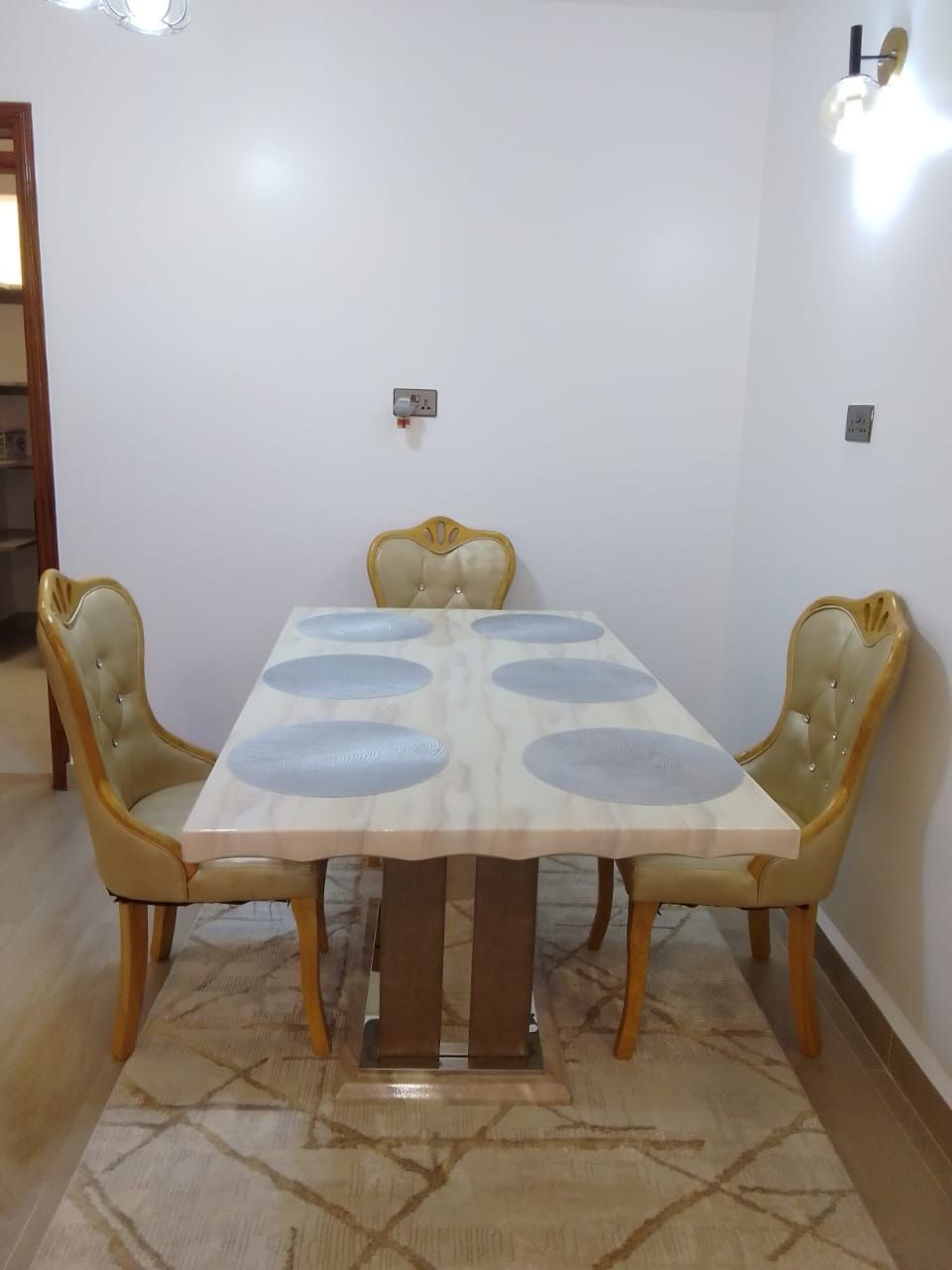 Une table à manger avec quatre chaises, un tapis à motifs et un luminaire fixé au mur.