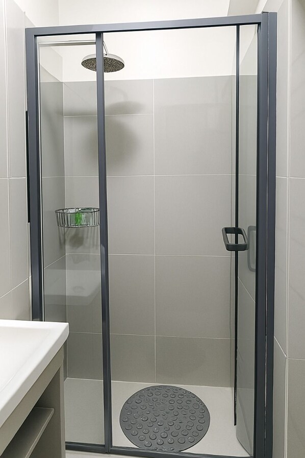 Une douche à l’italienne avec une porte en verre, un pommeau de douche et une petite étagère.