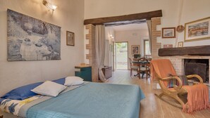A bedroom with a bed, a wooden rocking chair, a fireplace, and a dining area with a table and chairs. - Tenuta Focaioni - Monte Amiata (Stribugliano)
