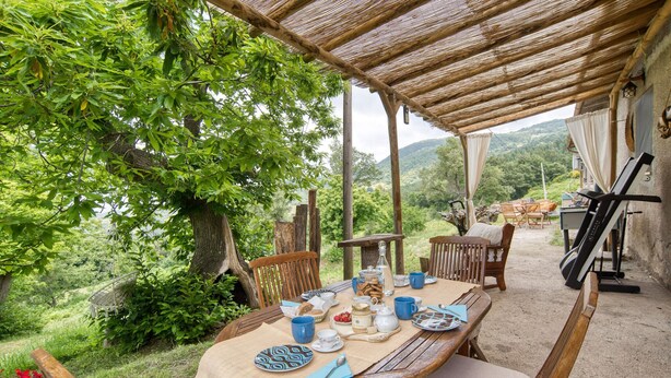 An outdoor dining area with a table set for two, surrounded by wooden chairs, under a thatched roof. - Tenuta Focaioni - Monte Amiata (Stribugliano)