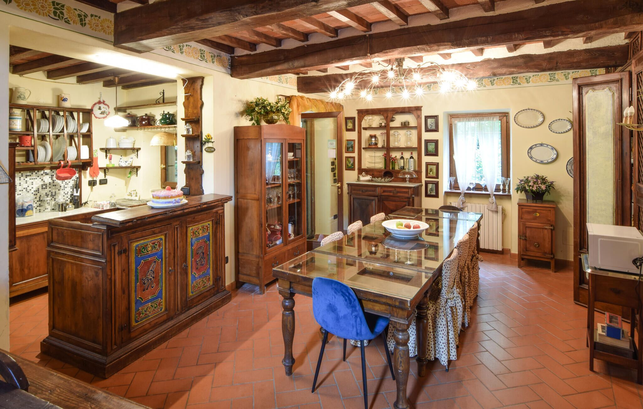 A traditional kitchen with wooden cabinets, a glass dining table, and a tiled floor.