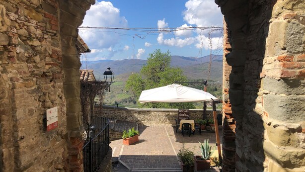 A stone-walled courtyard with a white umbrella table, potted plants, and a sign for "OSCARI Ristorante" against a backdrop of mountains and a clear sky. - Pet friendly apartment (Monte S.Maria Tiberina)