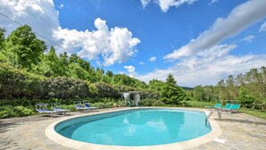 Ein kreisrunder Swimmingpool mit Liegestühlen und einem Pavillon, umgeben von üppiger Vegetation und Bäumen.