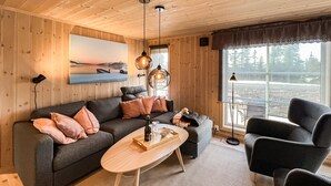 L’intérieur d’un chalet chaleureux, avec un canapé gris foncé, une table basse en bois et une vue sur un paysage enneigé par une grande fenêtre.