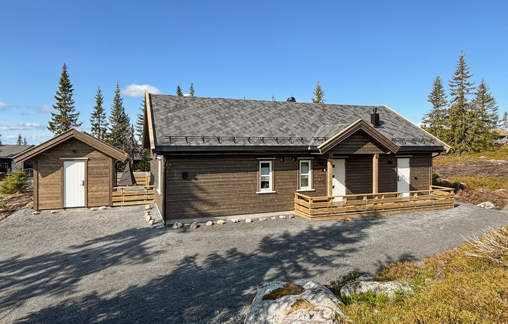 Une cabane en bois à deux étages, avec un toit en pente, une véranda à l’avant et un petit abri attenant.