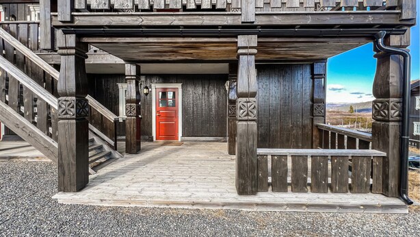 A wooden building with a red door, a staircase, and a view of the landscape.