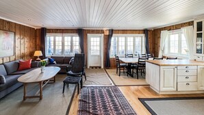 A cozy room with wooden walls, a sofa, a table, and a kitchen area with a dining table and chairs.