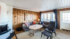 A cozy living room with a wooden wall, a sofa, a chair, a round table, and a fireplace.