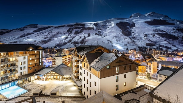 A snow-covered mountain at night with a bright star in the sky. There are buildings with balconies and a pool area in the foreground. - Apartment in Les Deux Alpes With Mountain Views (Les Deux Alpes)