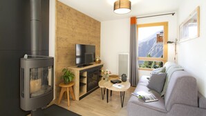 A modern living room with a fireplace, a television, a sofa, and a view of mountains through a window. - Apartment in Les Deux Alpes With Mountain Views (Les Deux Alpes)