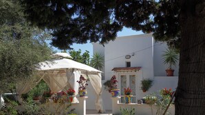 A courtyard with a white building, potted plants, and a canopy. - Romantic Trullo for 2  sea view pool,peaceful garden rustic  authentic Puglia (Carovigno)