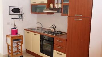 Una cucina compatta con mobili in legno, un fornello a gas, un microonde e un piccolo lavello.
