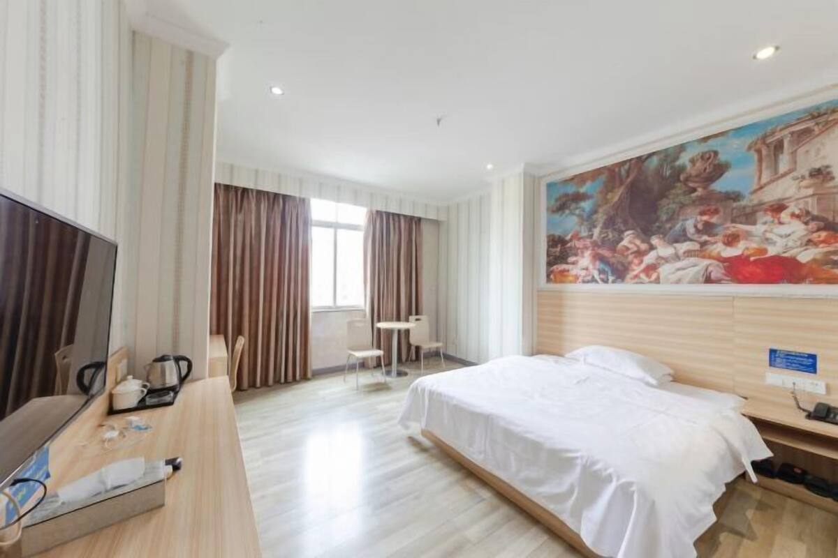 Une chambre d’hôtel avec un lit, une télévision, un bureau avec une chaise, une petite table et un tableau au mur.