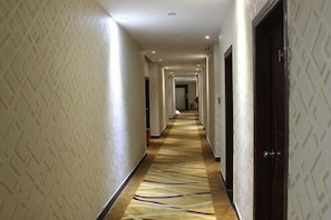 A hotel corridor with patterned walls, a carpeted floor, and doors leading to rooms.