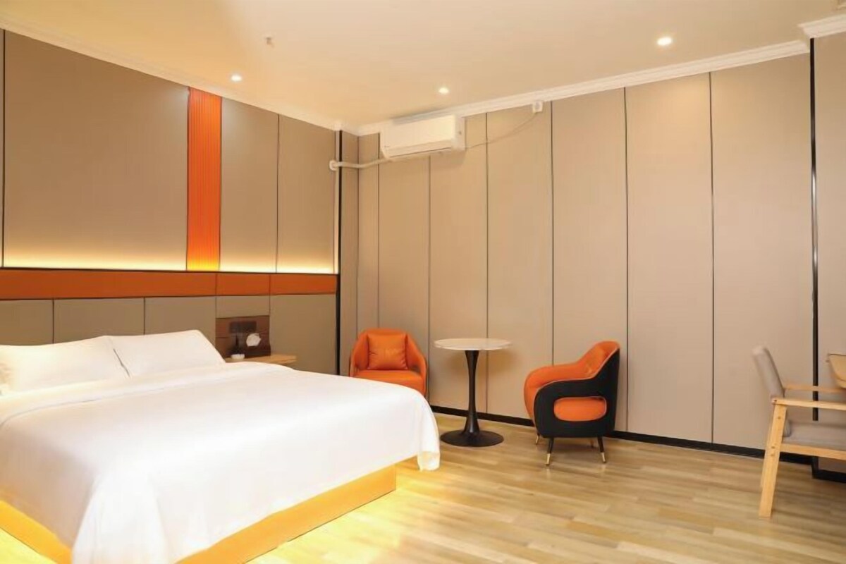 Une chambre d’hôtel avec un grand lit, une petite table, deux chaises et un climatiseur fixé au mur.