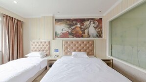 Habitación de hotel con dos camas individuales, un ventanal grande con cortinas, un cuadro sobre las camas y una mesita de noche de madera con un teléfono.