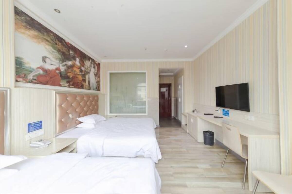 Une chambre d’hôtel avec deux lits, une télévision, un bureau et un tableau au mur.