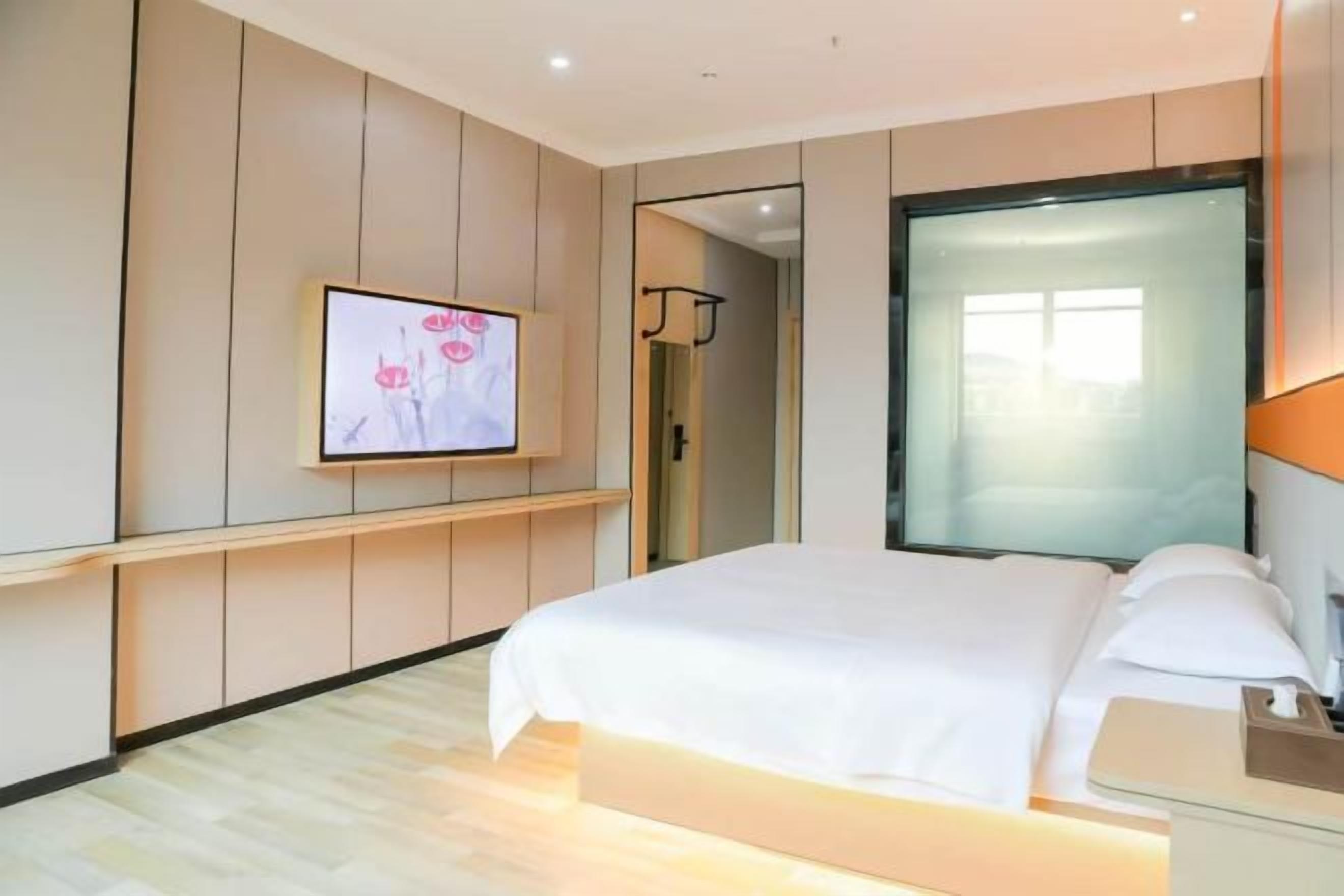 A hotel room with a bed, a TV mounted on the wall, and a window.