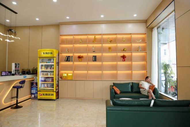 A hotel lobby with a reception desk, a vending machine, a green sofa, and a wall with shelves.